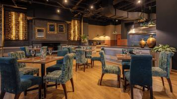Un restaurant avec des tables en bois et des chaises à coussins bleus, un coin bar et des appliques murales décoratives.