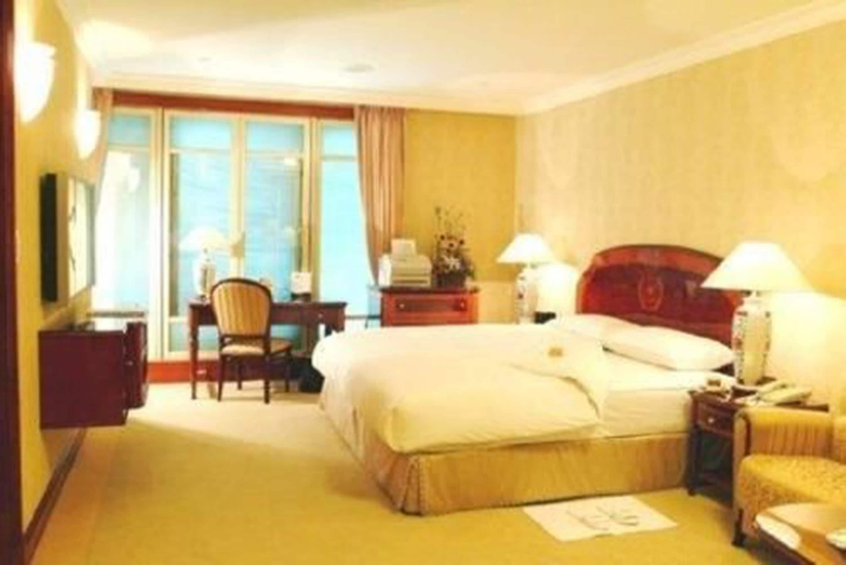 Habitación de hotel con una cama grande, dos lámparas de noche, un escritorio con silla y una ventana con cortinas.