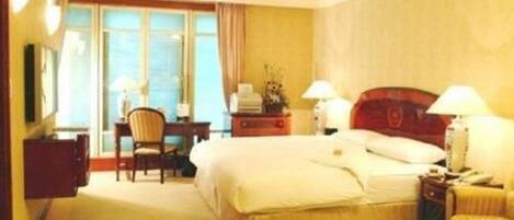 Habitación de hotel con una cama grande, dos lámparas de noche, un escritorio con silla y una ventana con cortinas.