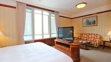 A hotel room with a large bed, a television on a wooden stand, a sofa, and a painting on the wall.