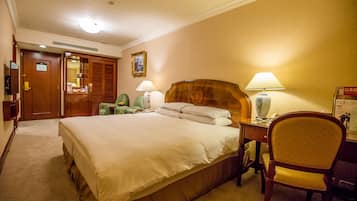 A hotel room with a large bed, two bedside tables with lamps, a wooden headboard, a chair, and a desk with a lamp.