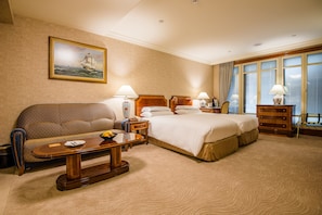 A hotel room with a large bed, a sofa, a wooden coffee table, and a painting on the wall.