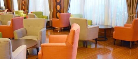 Een hotel lobby met verschillende zithoeken, waaronder oranje en groene stoelen, en een houten vloer.