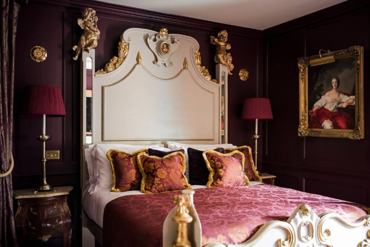Um quarto luxuoso com uma cama grande, cabeceira elaborada e um retrato clássico na parede.