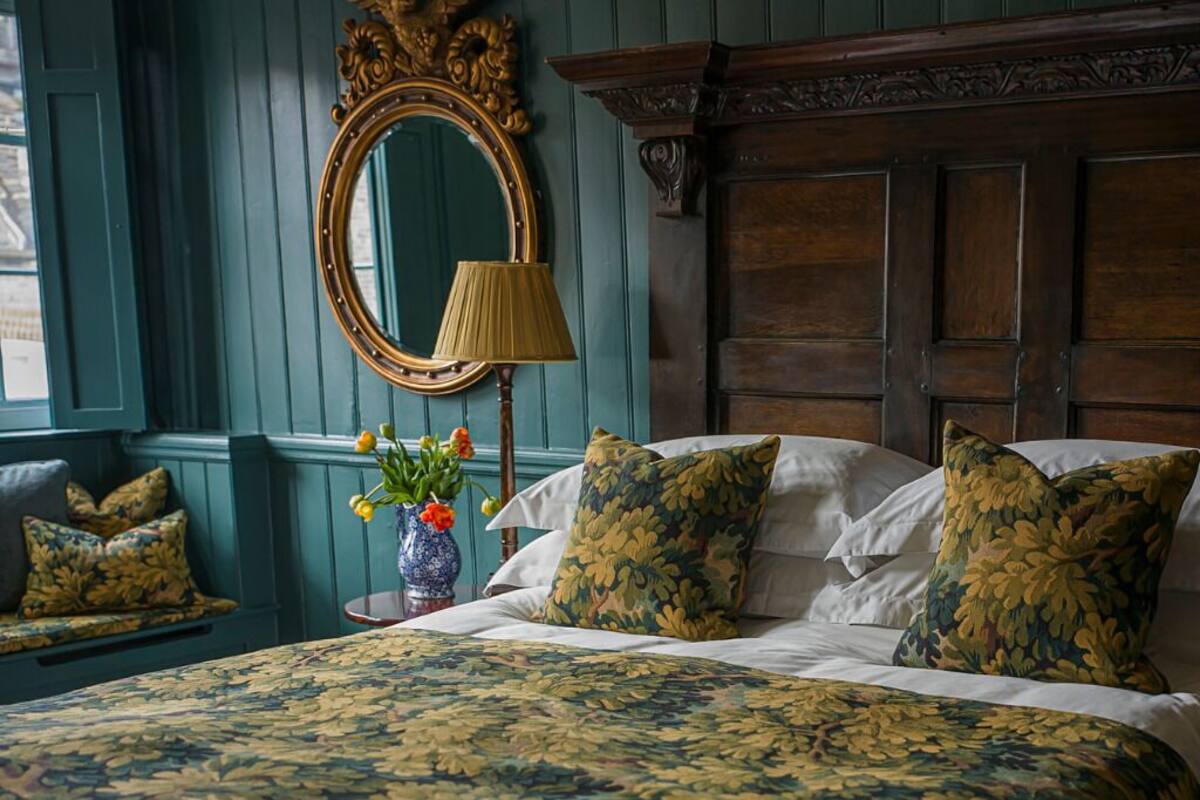 Quarto com colcha florida, espelho redondo e cabeceira de madeira.
