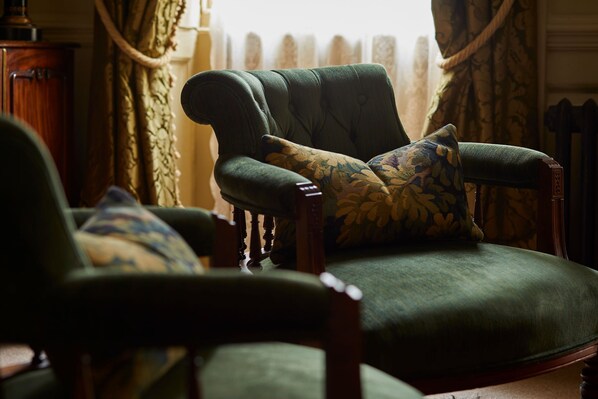 A green armchair with a floral pillow in a room with curtains and a wooden cabinet.