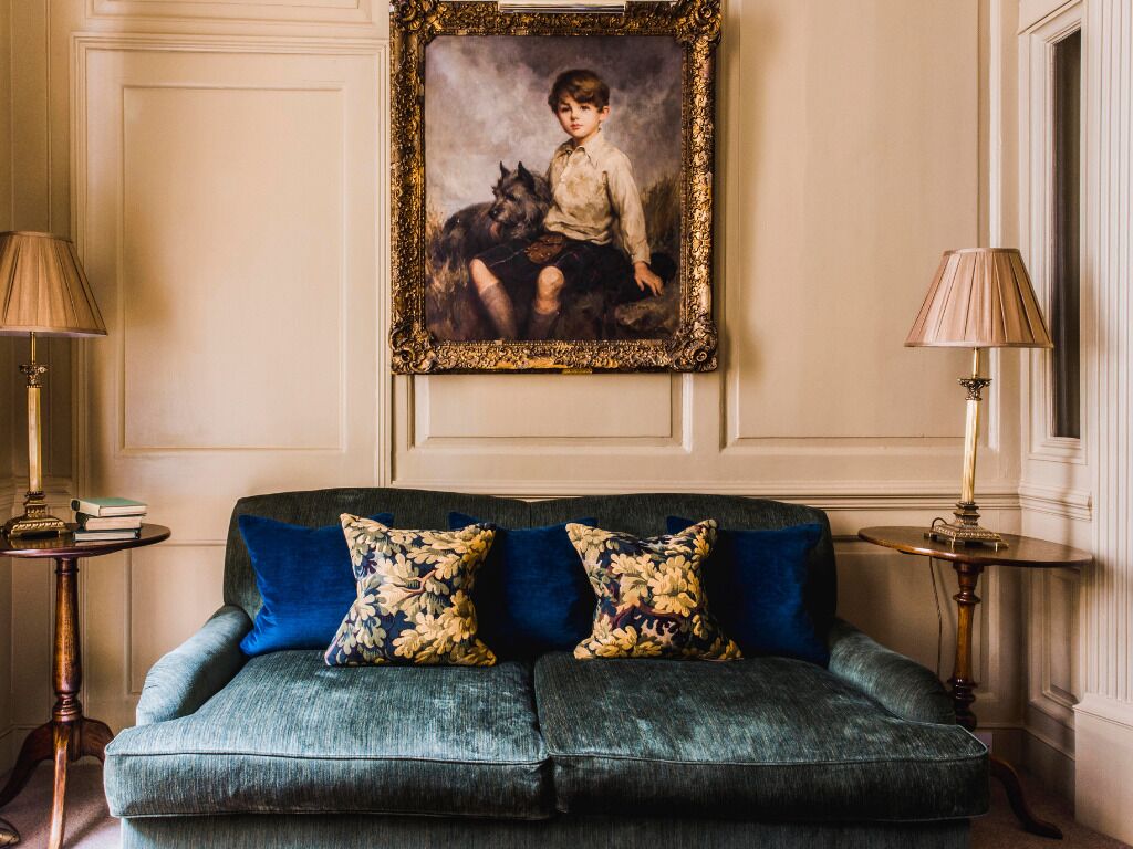Una habitación con un sofá verde oscuro, dos almohadones florales a juego, un retrato enmarcado en la pared y dos mesitas de noche con lámparas.