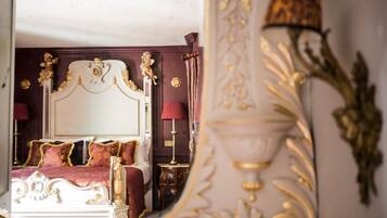 A luxurious bedroom with an ornate bed, a mirror reflecting the room, and a decorative lamp.