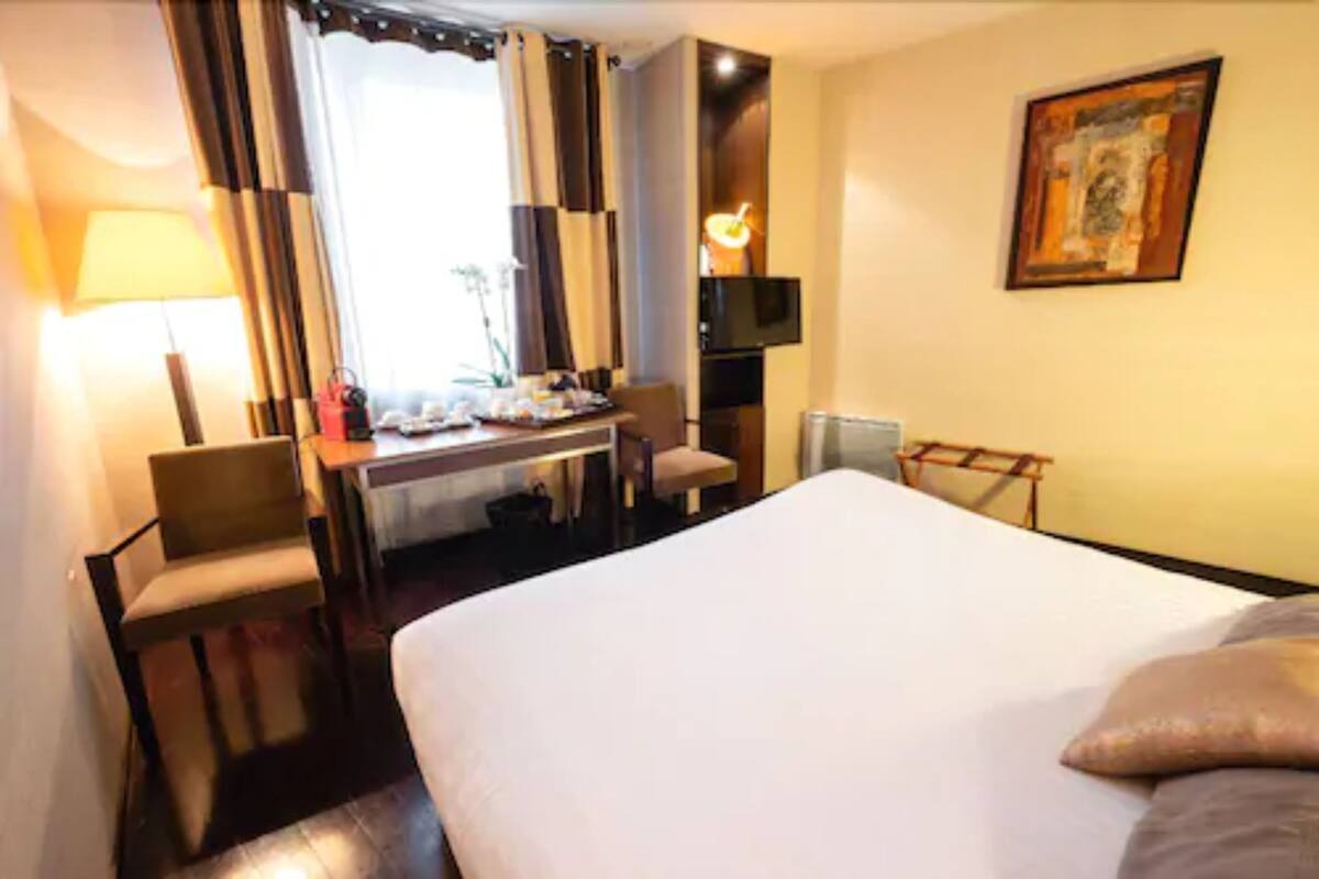 Une chambre d’hôtel avec un grand lit, un bureau avec une chaise, une télévision et un tableau au mur.