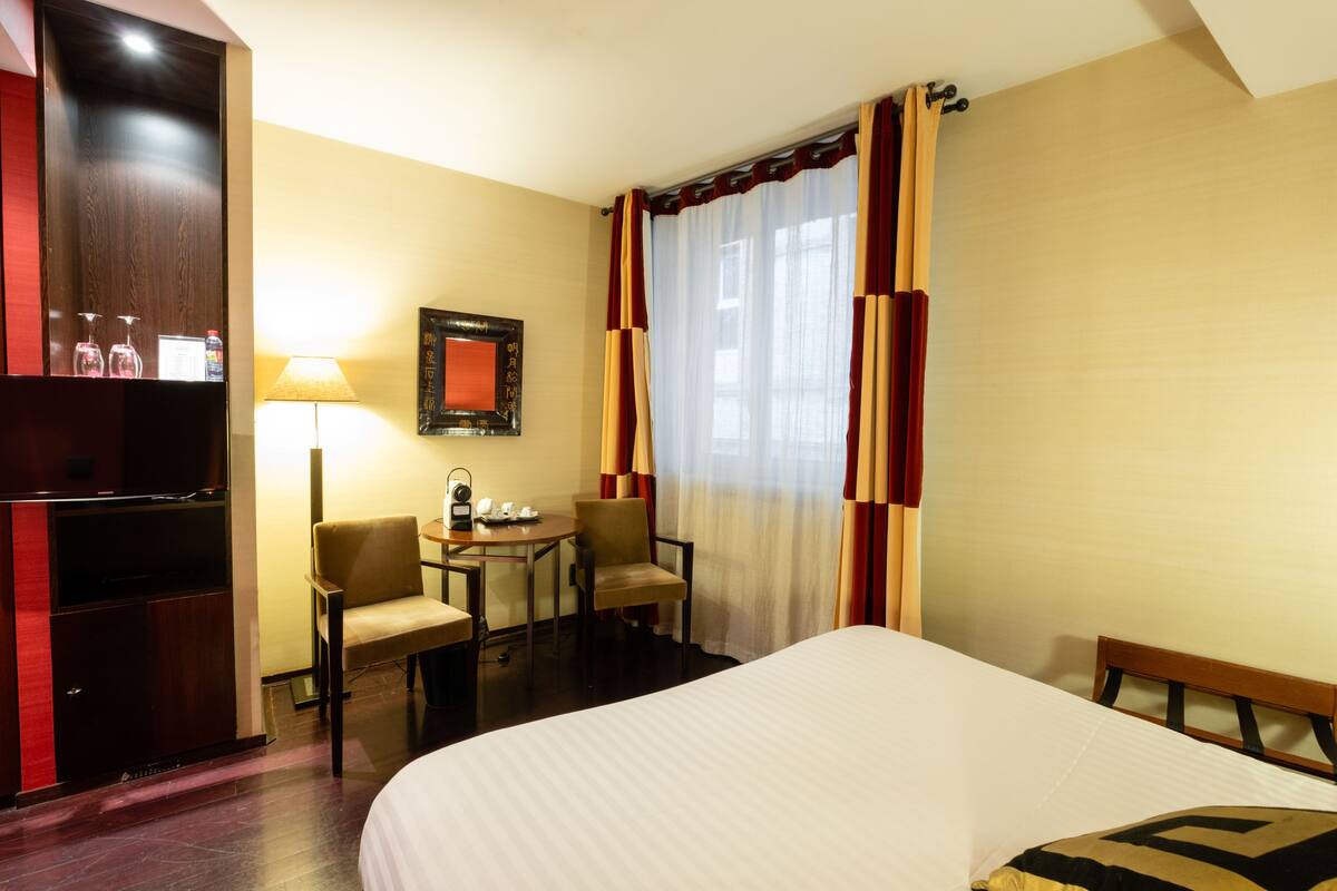 Une chambre d’hôtel avec un lit, un bureau avec une chaise, une lampe et un téléviseur posé sur un meuble.