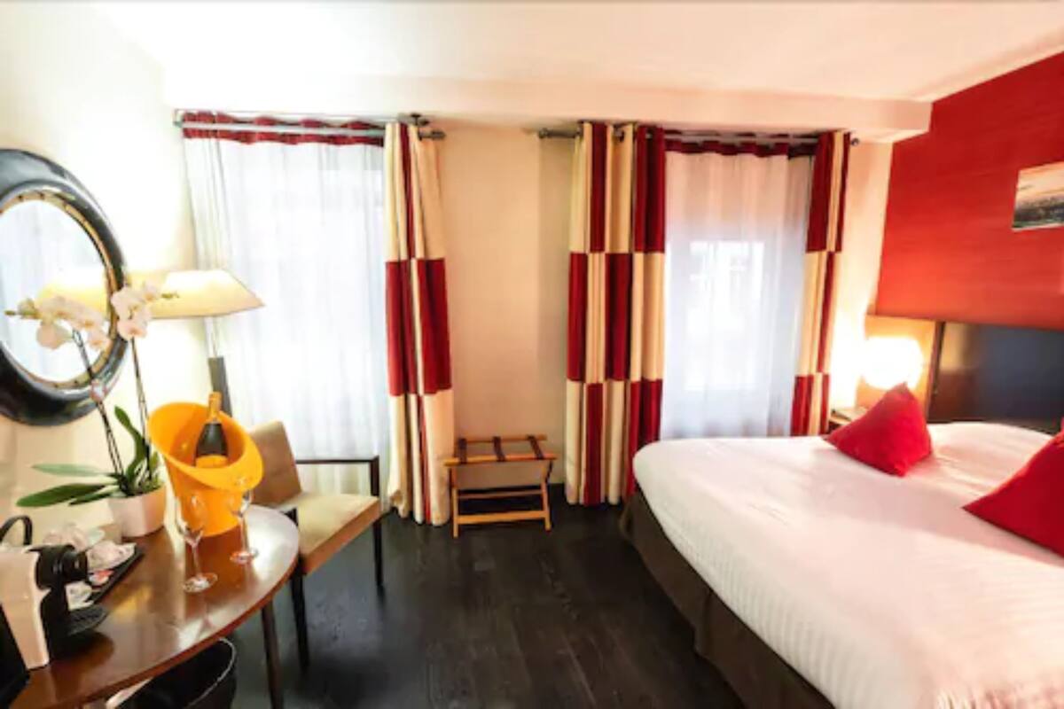 Une chambre d’hôtel avec un lit, un bureau doté d’une lampe, une chaise et une petite table sur laquelle se trouvent une plante et une bouteille.