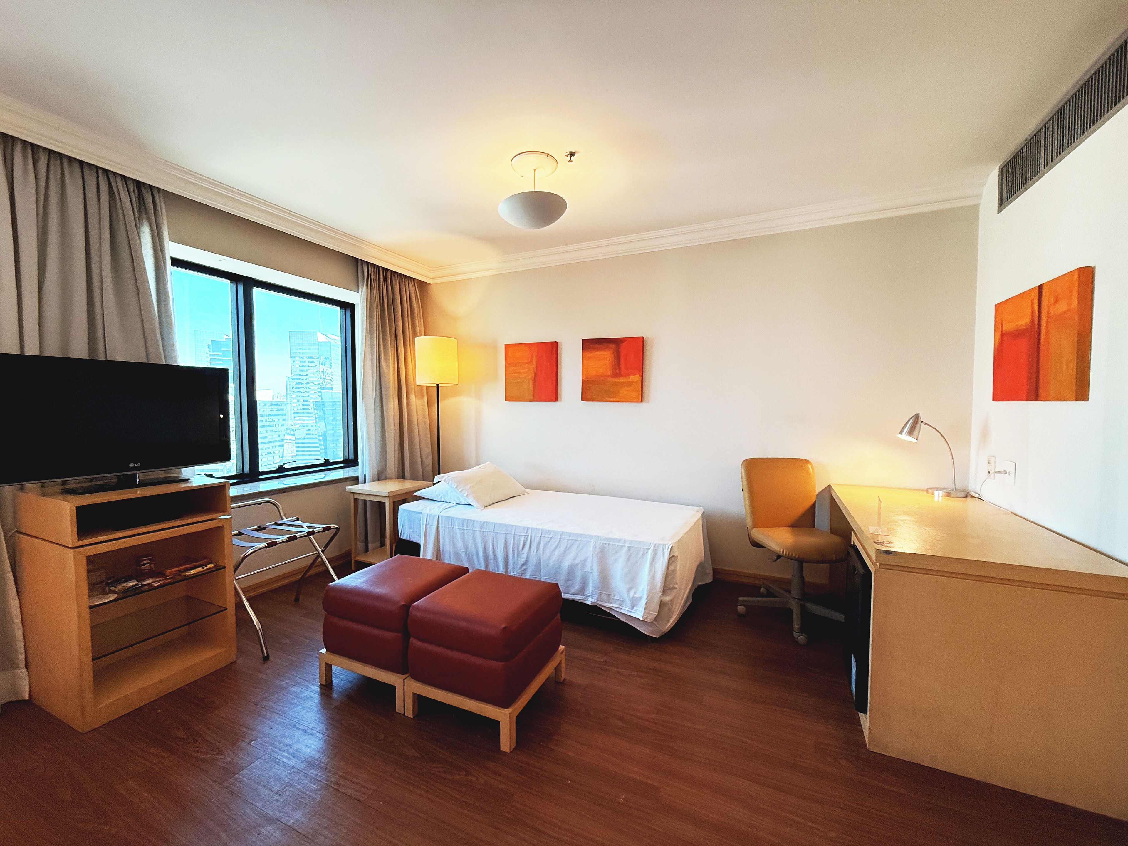A hotel room with a bed, a desk, a chair, a TV, and a window with curtains.