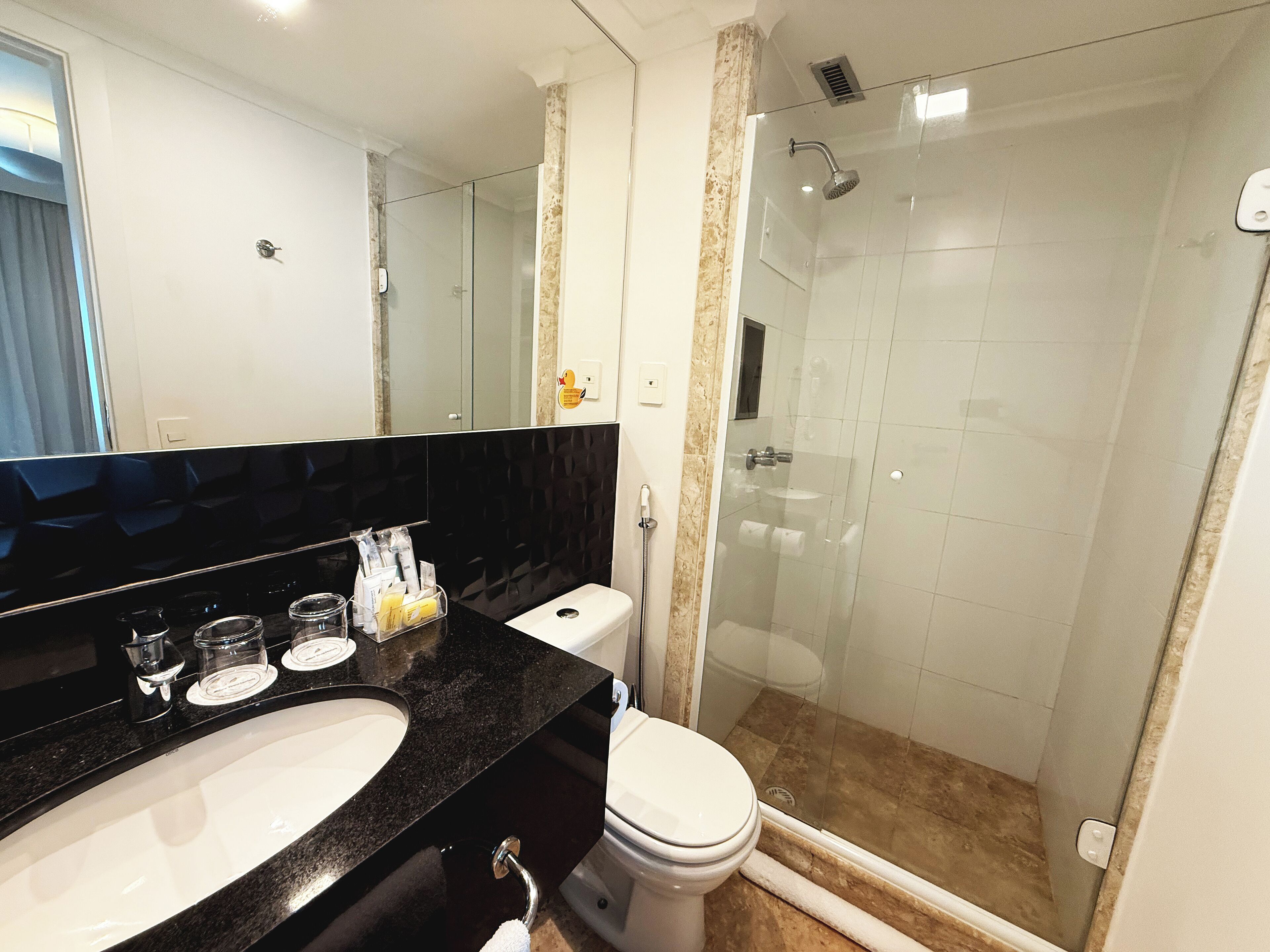 A modern bathroom with a black countertop, white sink, and a glass-enclosed shower.
