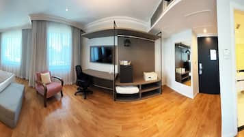 A modern hotel room with a bed, a desk, a chair, a TV, and a bathroom.