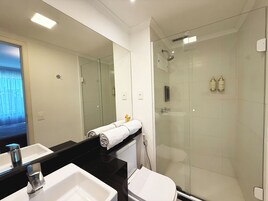 Un bagno moderno con doccia vetro, lavandino bianco e piano di appoggio nero.