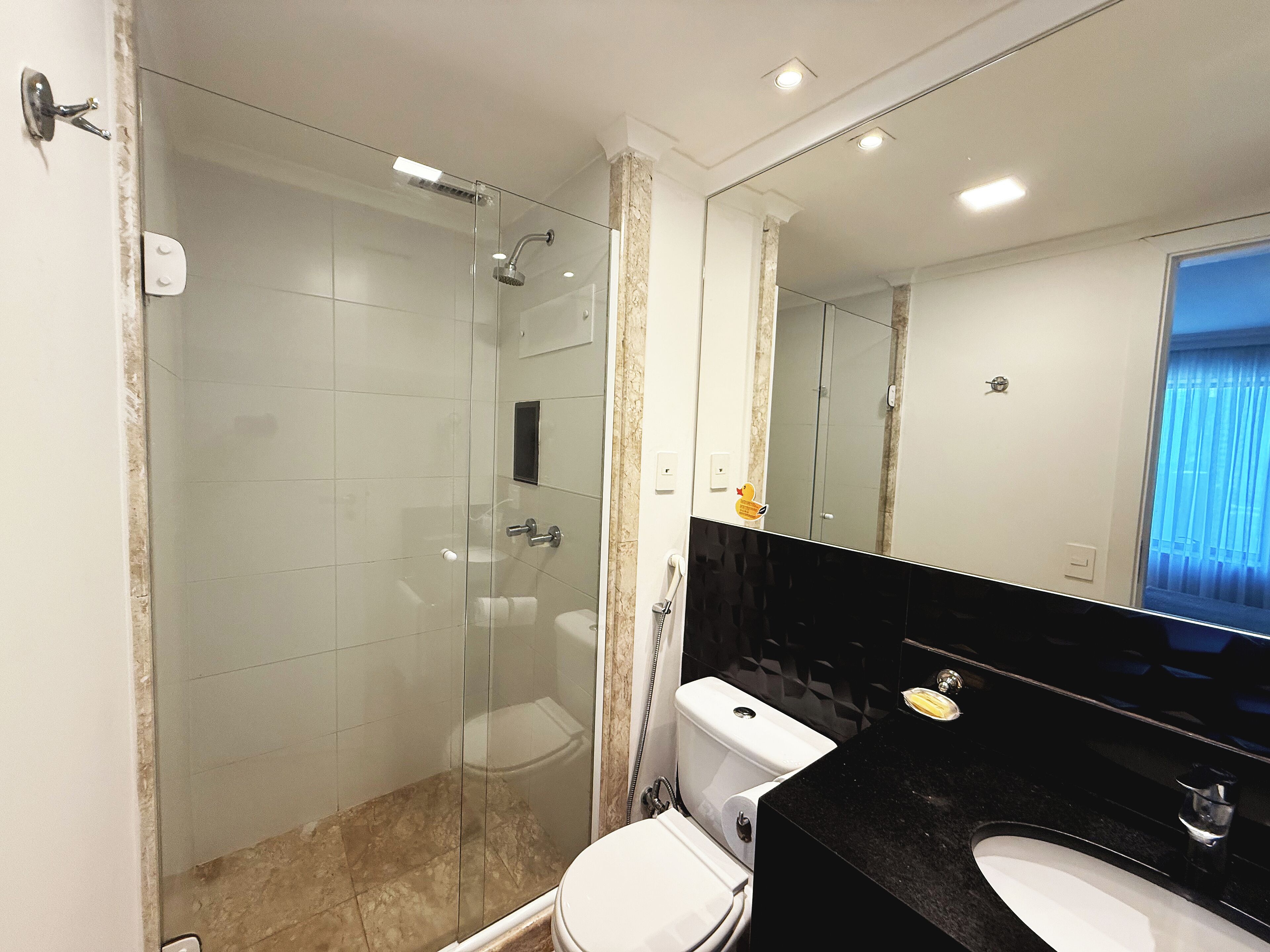 Un baño moderno con ducha de vidrio, inodoro blanco y lavamanos negro con un espejo grande.
