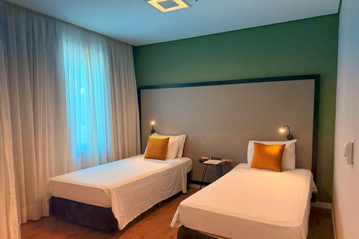 A hotel room with two single beds, a small table, and a chair.