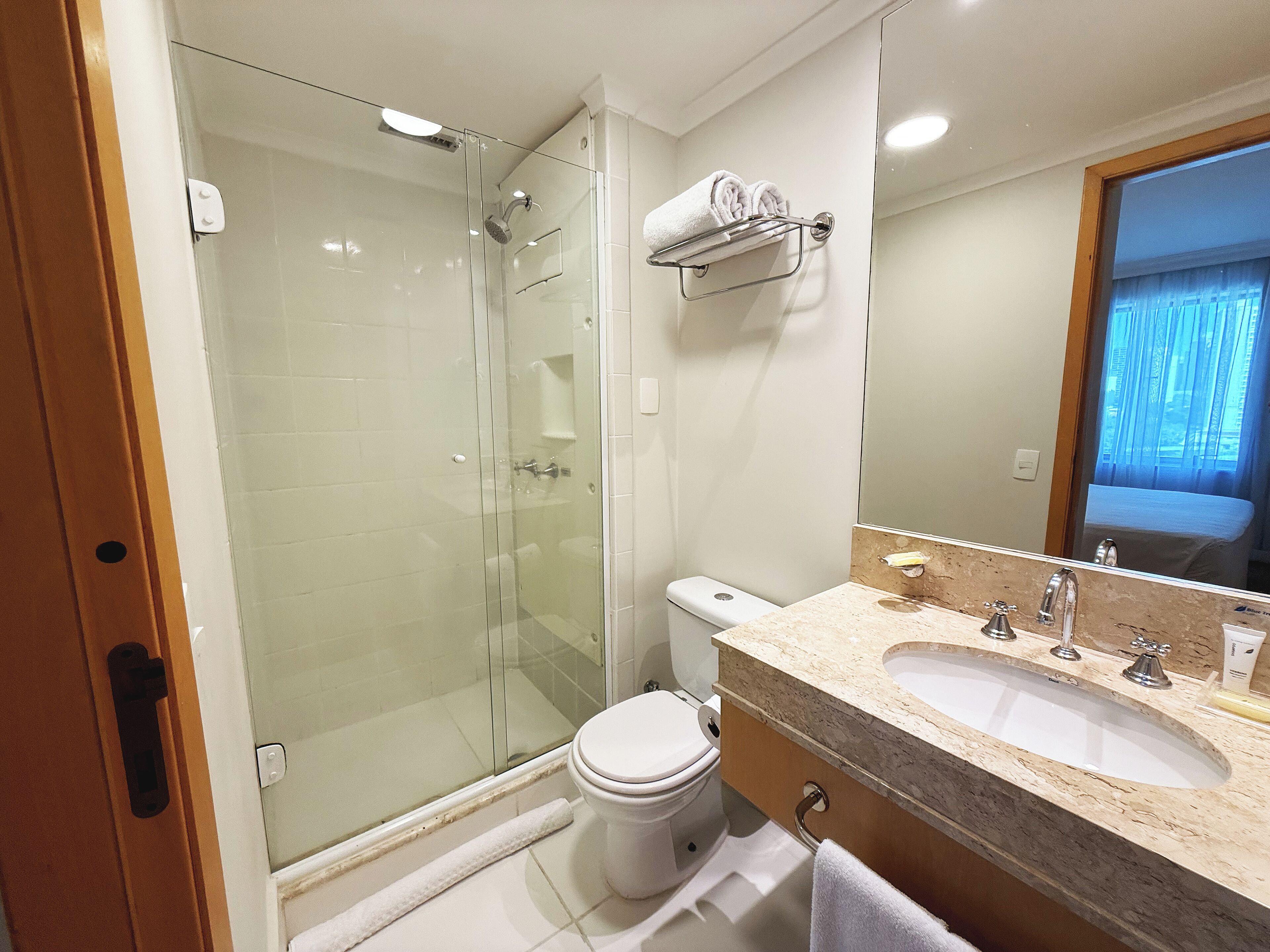 A modern bathroom with a glass shower enclosure, a white toilet, and a marble sink with a mirror above it.