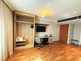 A hotel room with a wooden wardrobe, a desk with a chair, a television mounted on the wall, and a door with a motivational quote.