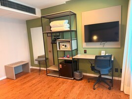 A compact room with a bed, a desk, a chair, a TV, and a shelving unit.