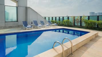 A rooftop pool with clear blue water, surrounded by lounge chairs and a modern architectural design.
