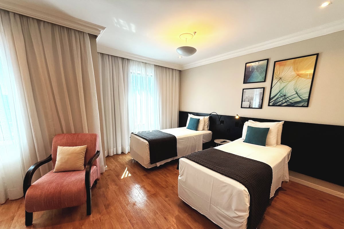 A hotel room with two beds, a chair, and a small table.