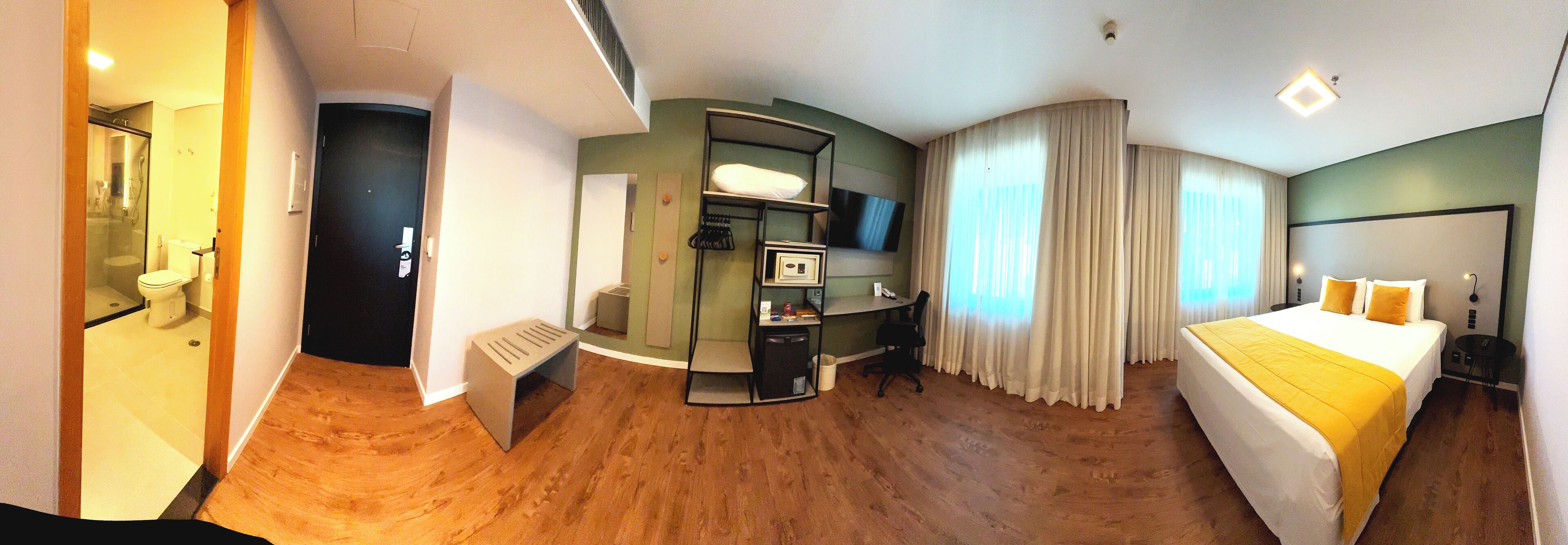 Habitación de hotel con cama, escritorio, silla, televisor y zona de ducha.