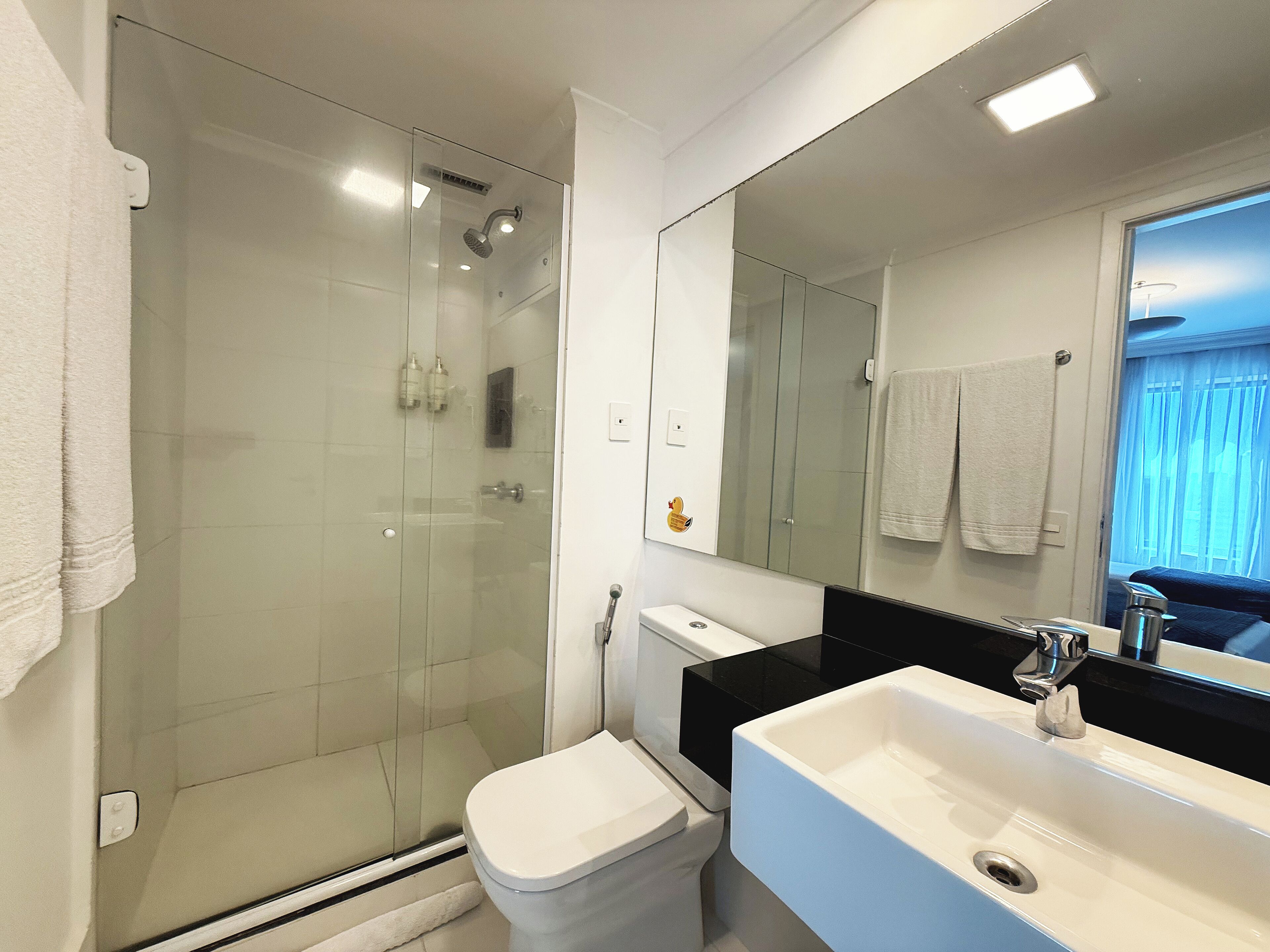Une salle de bain moderne avec une douche à parois de verre, des toilettes blanches et un grand lavabo doté d’un plan de travail noir.