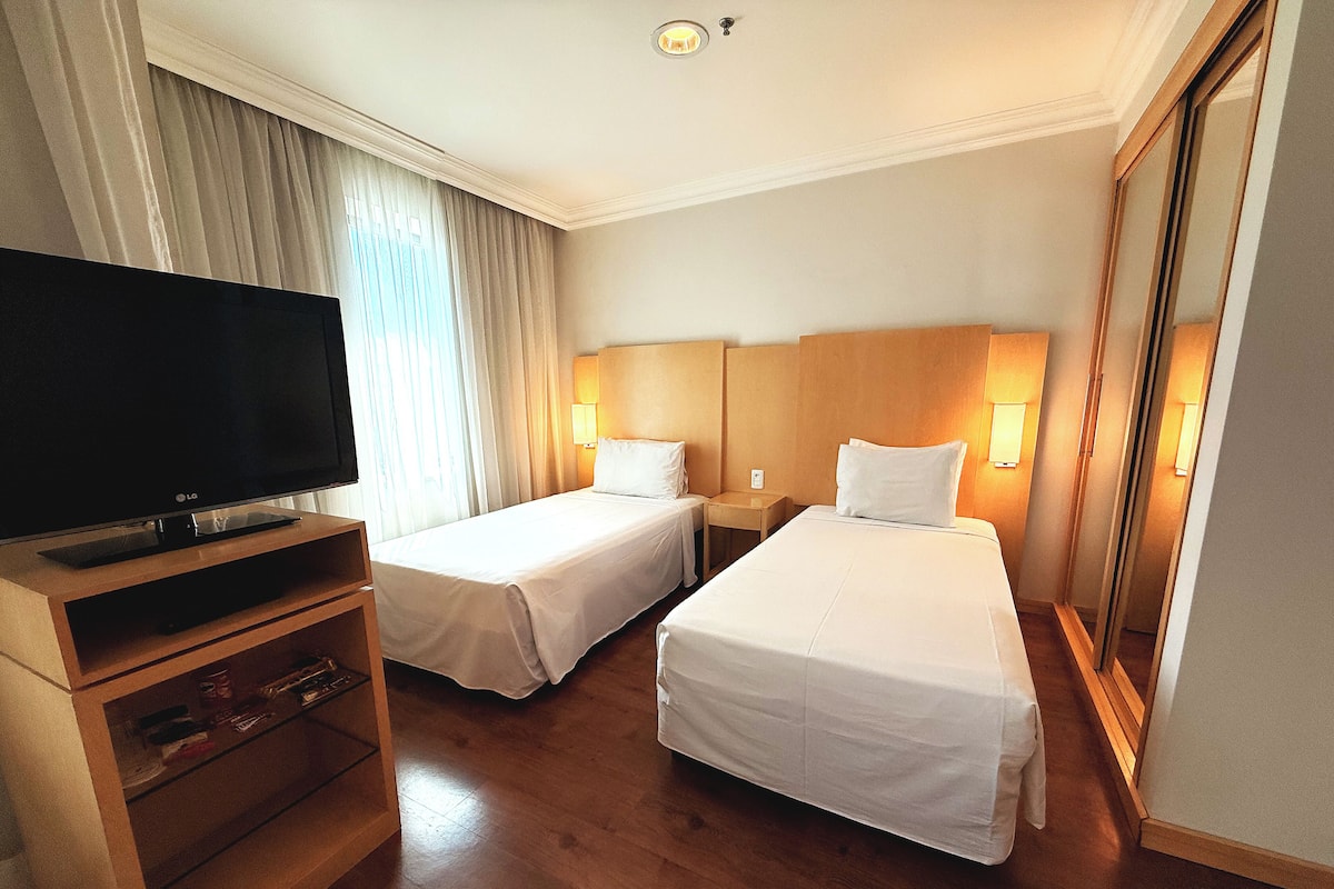 A hotel room with two beds, a TV, wooden flooring, and a mirror.