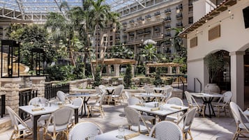 A hotel atrium with multiple dining areas, indoor and outdoor seating, and a central garden.