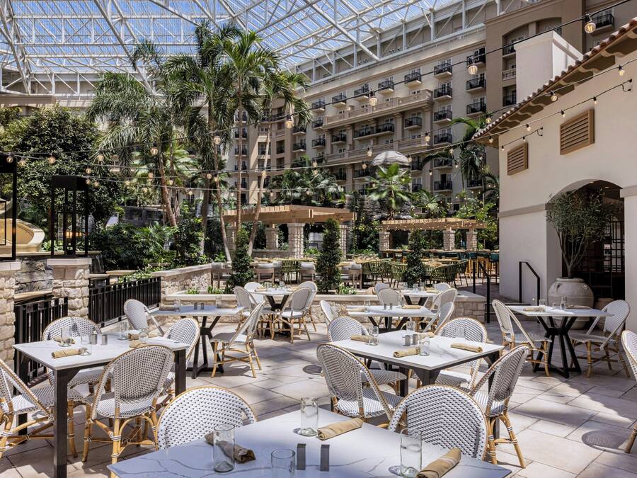 A hotel atrium with multiple dining areas, indoor and outdoor seating, and a central garden.
