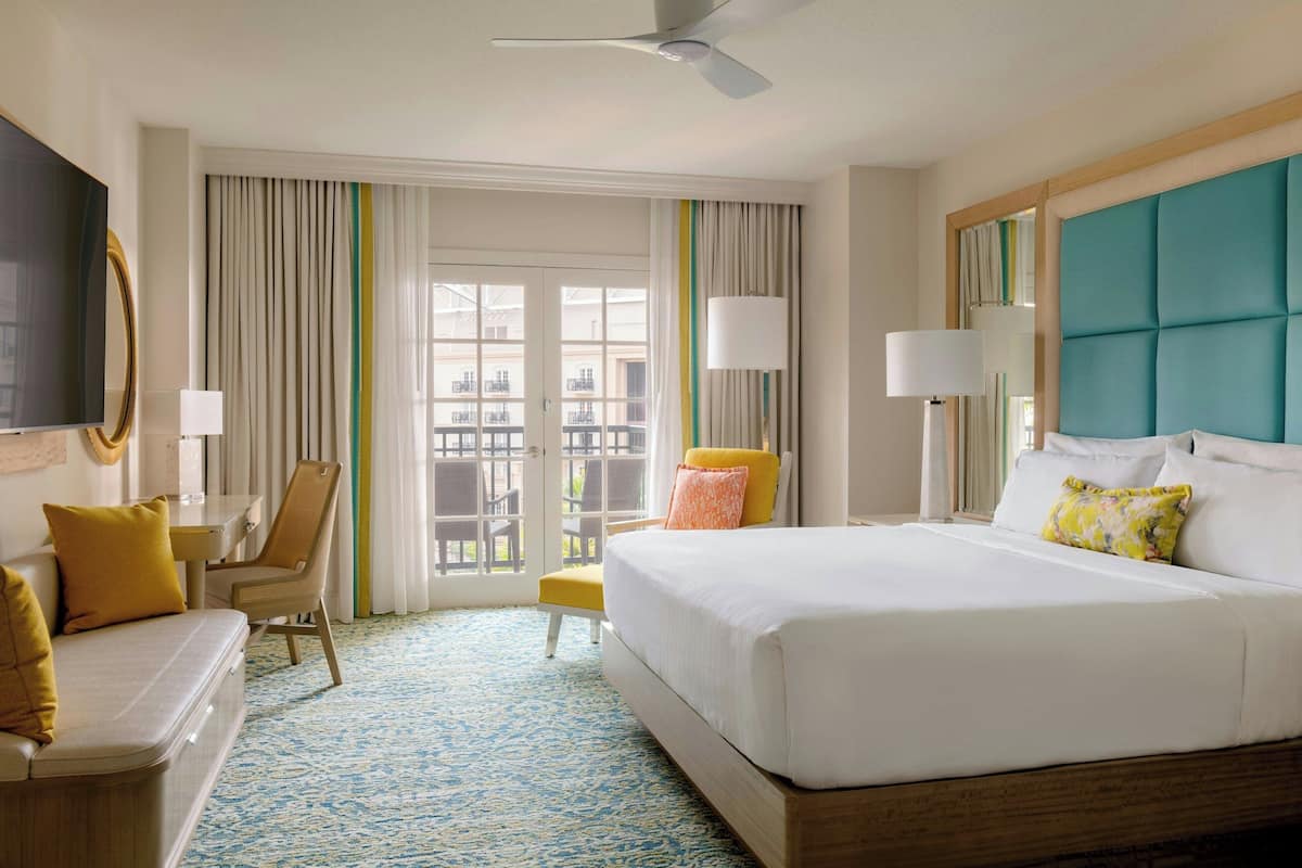 A hotel room with a large bed, a desk, a chair, and a balcony with curtains.