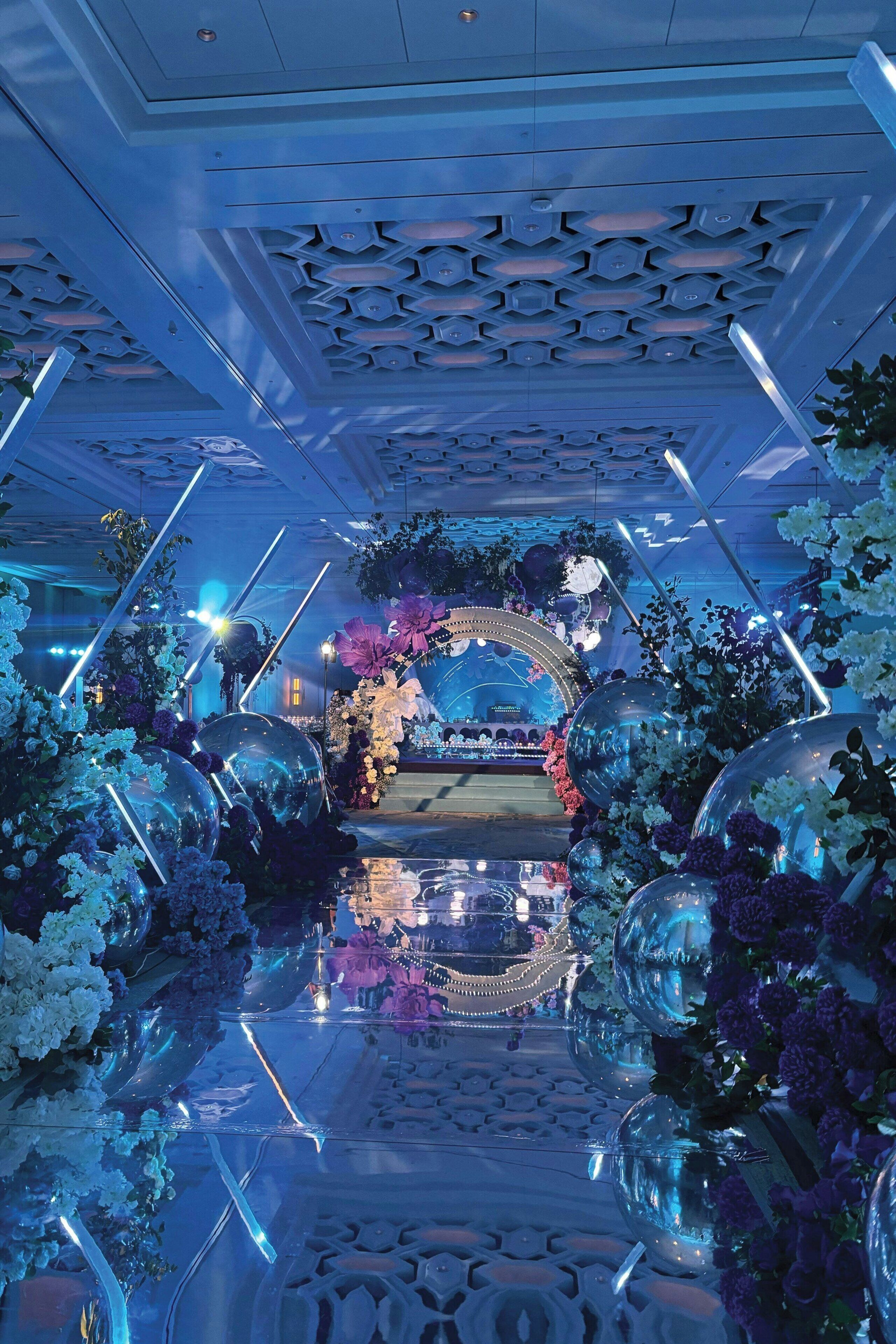 A venue with a reflective floor, decorative ceiling, and floral arrangements.