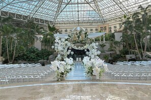 An indoor venue with a glass ceiling, rows of white chairs, and floral decorations. - Gaylord Palms Resort & Convention Center (Kissimmee)