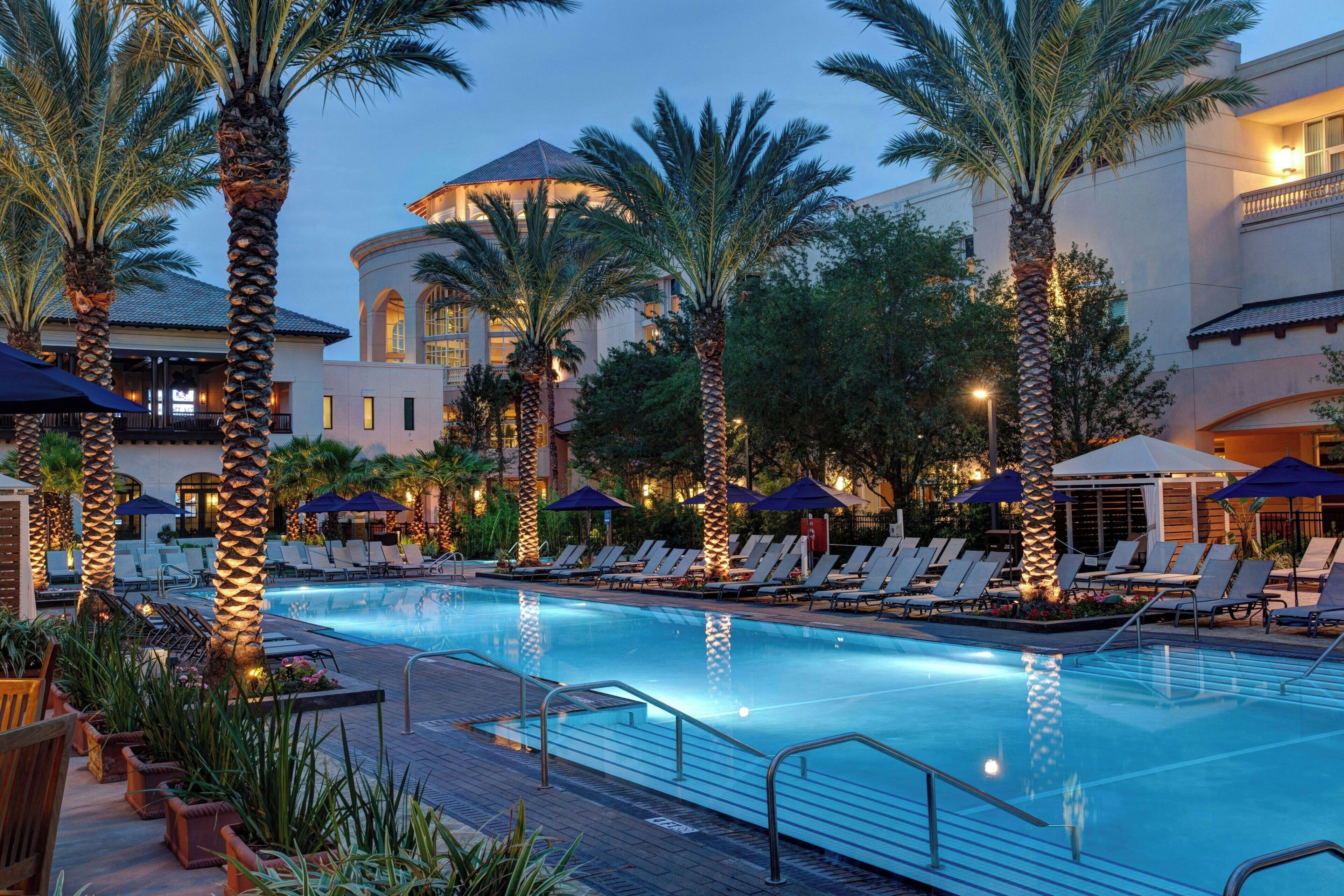 A pool area with lounge chairs and umbrellas, surrounded by palm trees and a building with a dome structure.