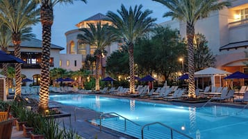 A pool area with lounge chairs and umbrellas, surrounded by palm trees and a building with a dome structure.