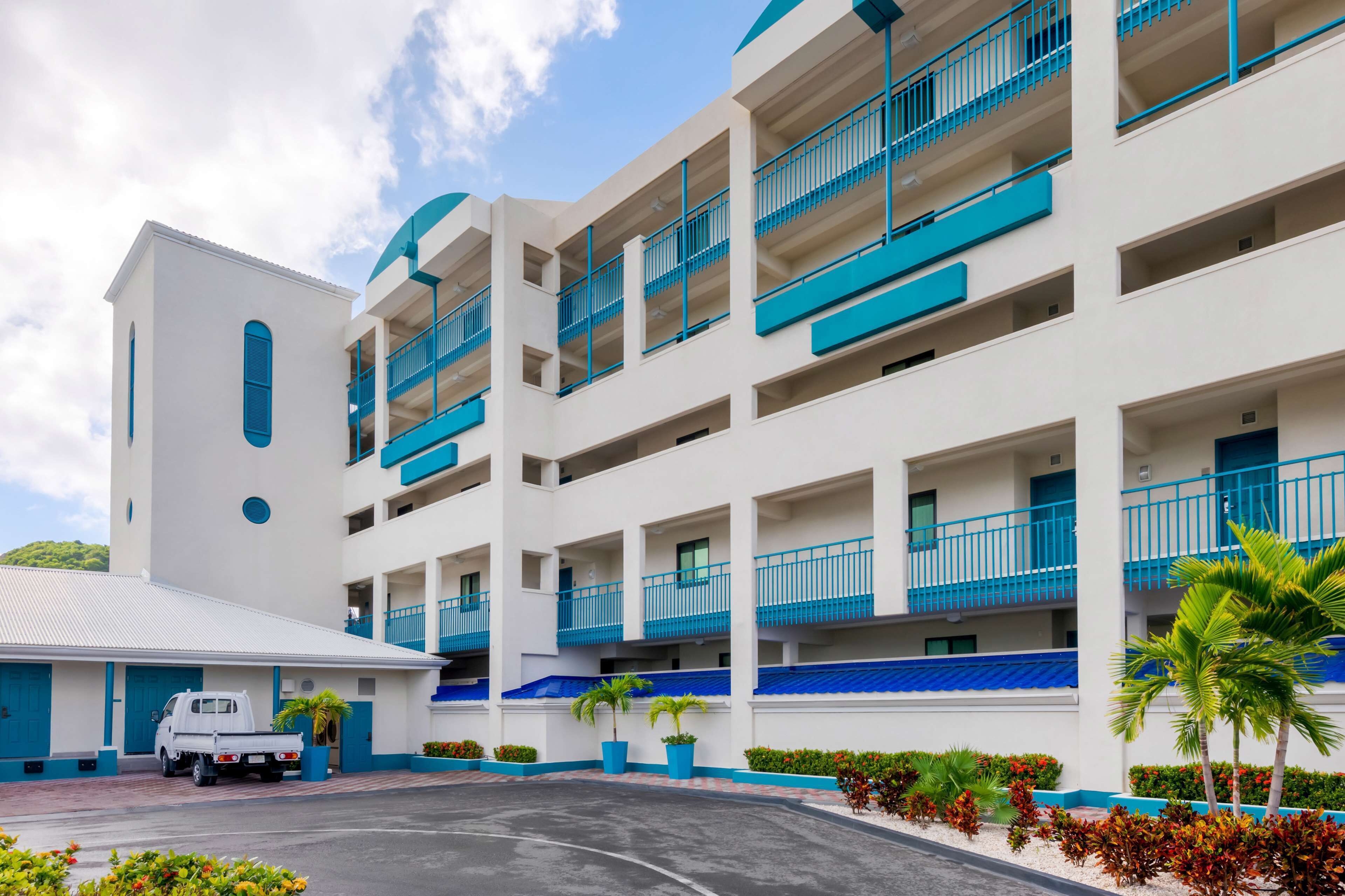 A multi-story hotel with balconies, a parking area, and landscaped gardens.