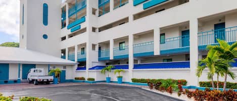 A multi-story hotel with balconies, a parking area, and landscaped gardens.
