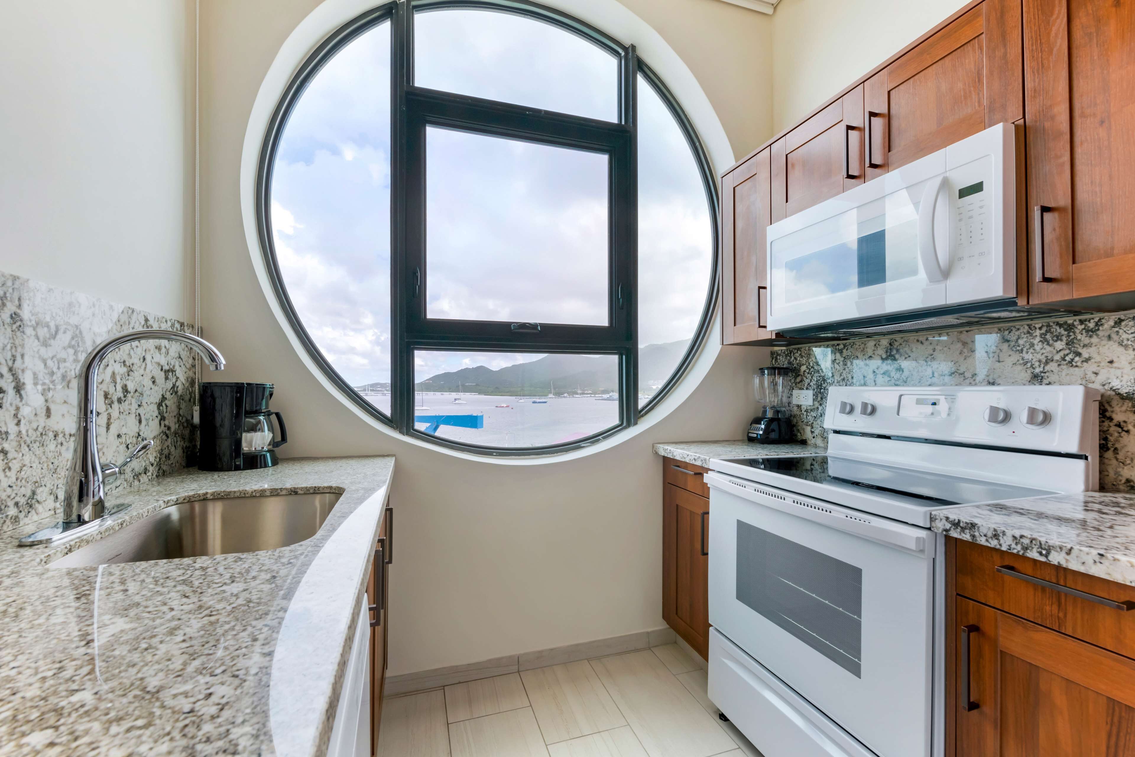 A kitchen with granite countertops, a stainless steel sink, a microwave, an oven, and wooden cabinets.