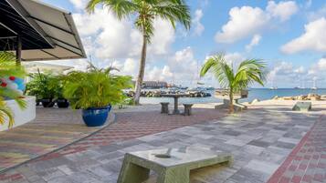 A patio area with a view of the sea, palm trees, and boats.