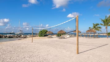 A beach volleyball court with a net, surrounded by palm trees and beach chairs.