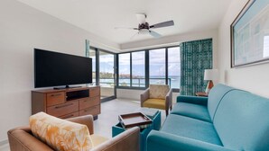 Een moderne woonkamer met een flatscreen televisie, een plafondventilator en een groot raam met uitzicht op de zee.