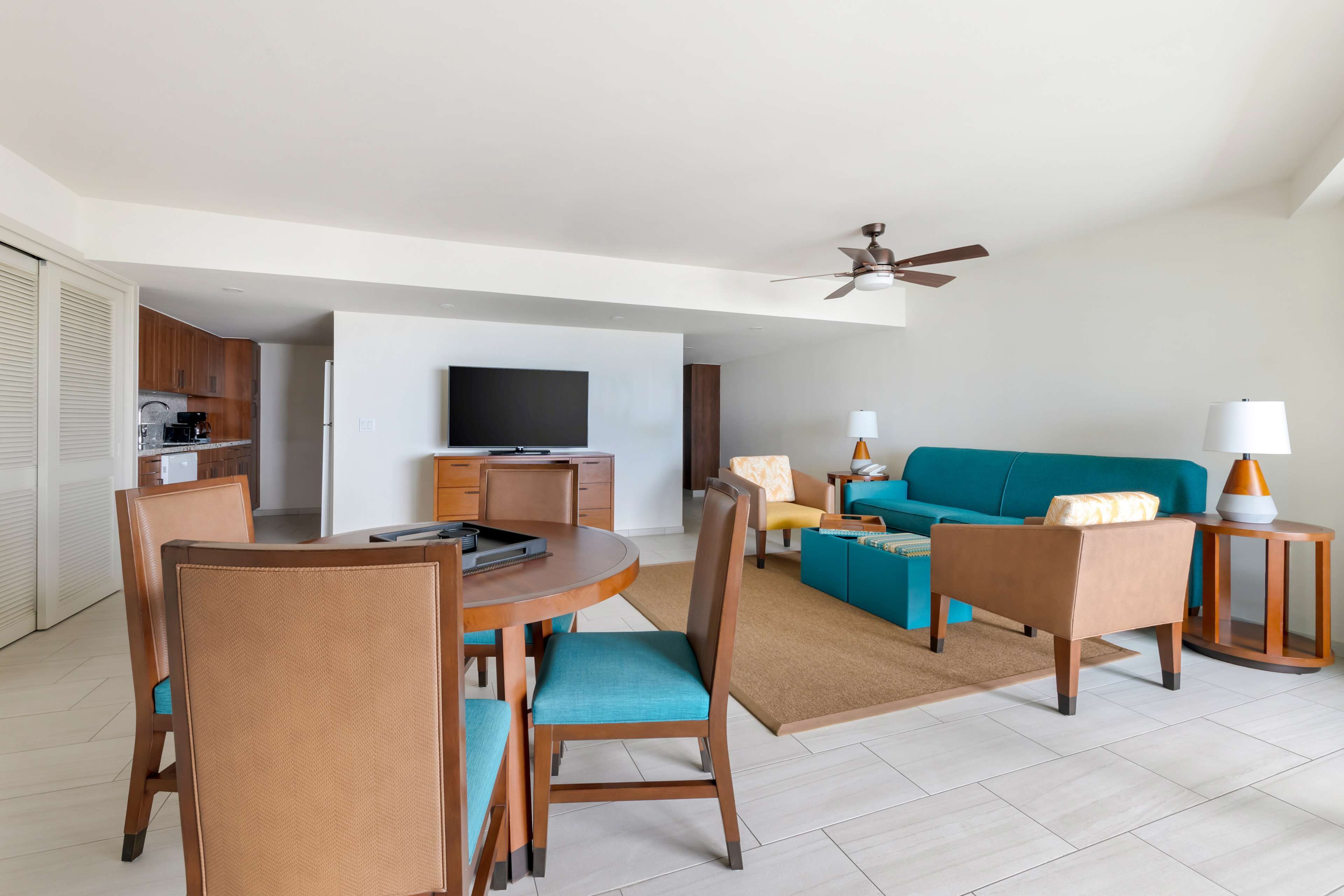 A modern living room with a sofa, chairs, a dining table, and a television.