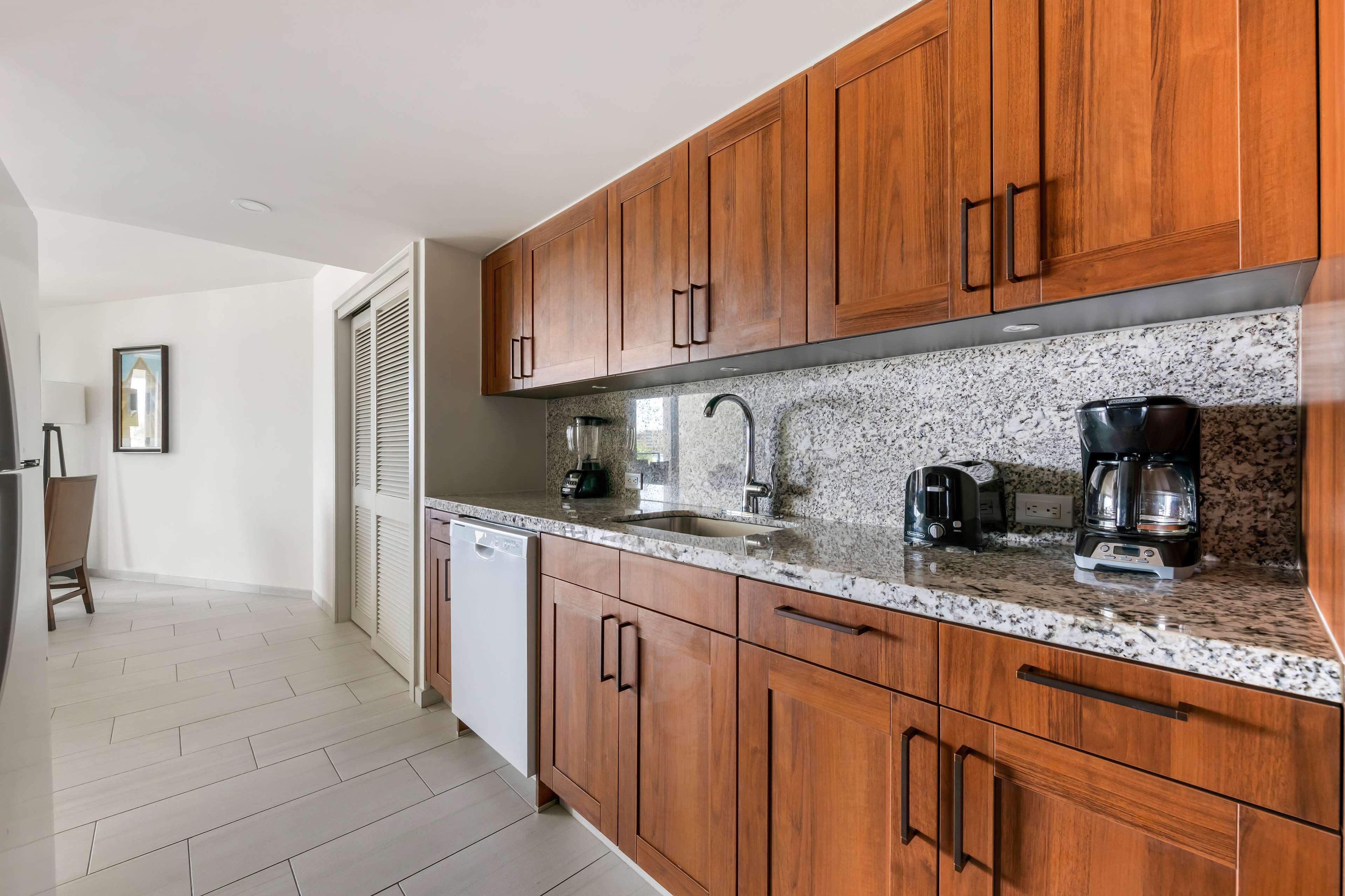 A modern kitchen with wooden cabinets, granite countertops, and stainless steel appliances including a coffee maker and toaster.