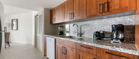 A modern kitchen with wooden cabinets, granite countertops, and stainless steel appliances including a coffee maker and toaster.