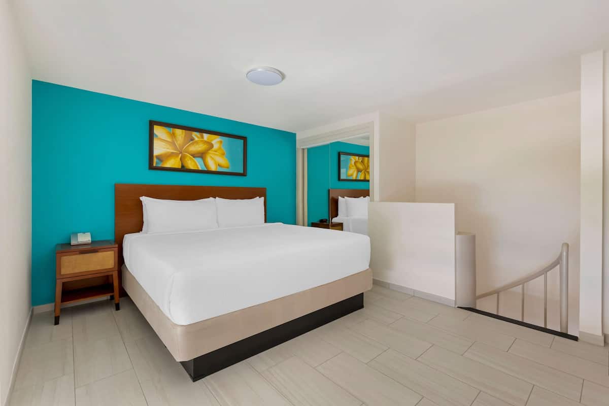 Ein Hotelzimmer mit einem großen Bett, einem Nachttisch, einem Spiegel und einer Tür mit Geländer.