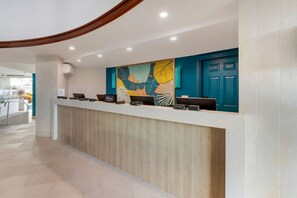 A hotel reception area with a wooden reception desk, a blue door, and a colorful abstract painting on the wall.