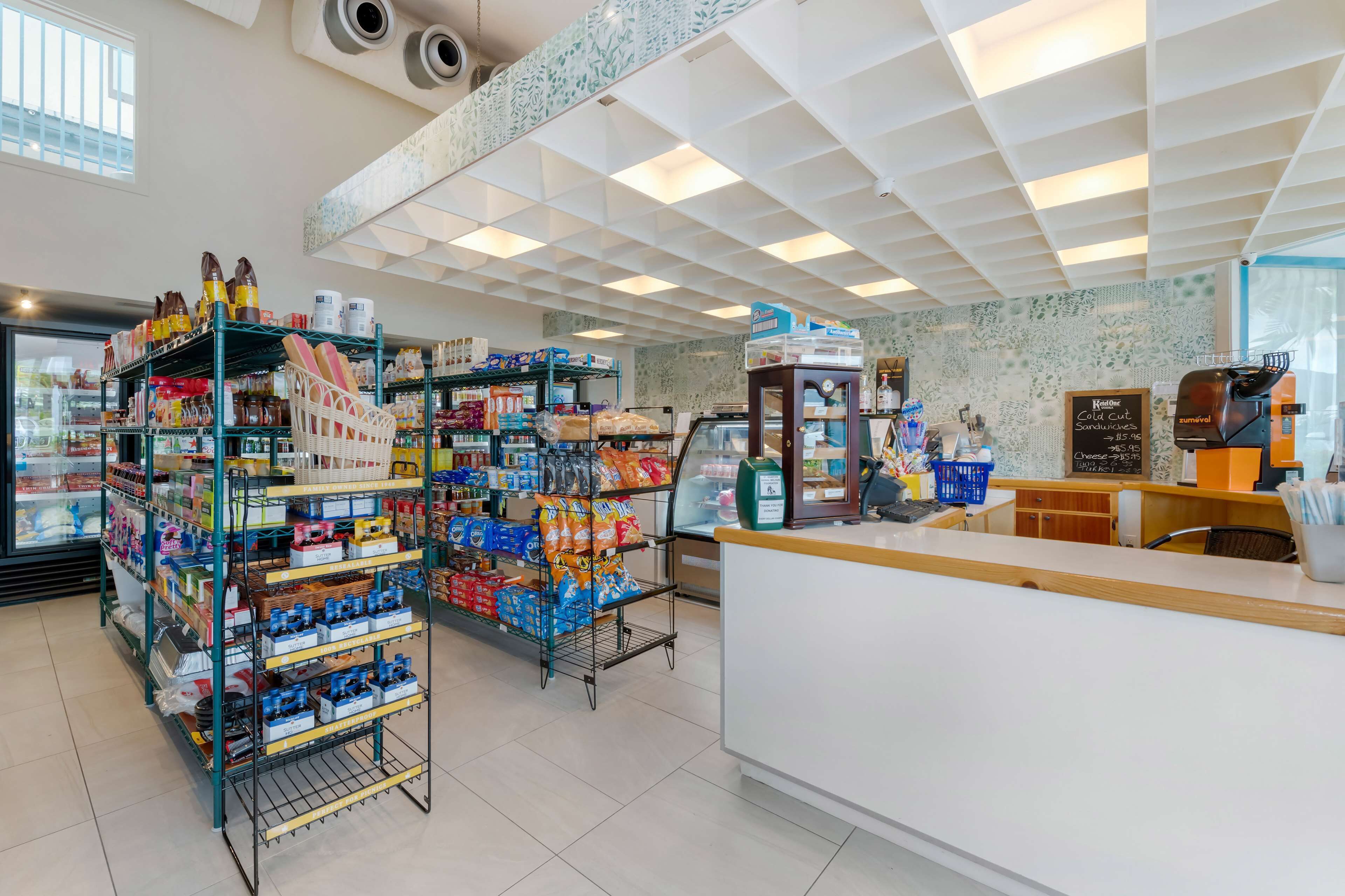Een net en overzichtelijk café met planken vol snacks en drankjes, een koffieapparaat en een krijtbordmenu.