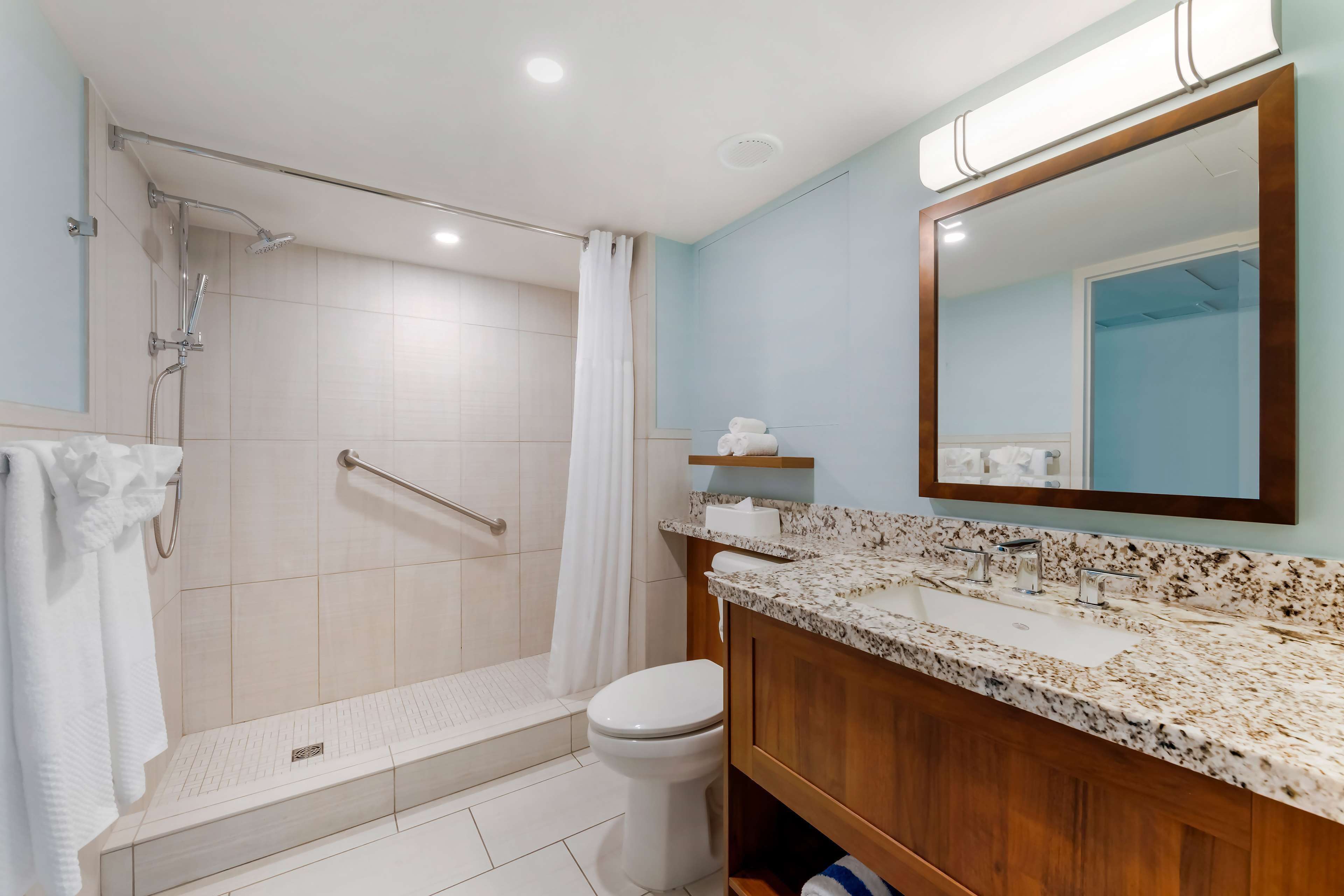 A modern bathroom with a walk-in shower, a toilet, a sink with a marble countertop, and a mirror above the sink.