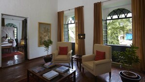 A room with two armchairs, a coffee table with books, a framed picture, and a potted plant. - Siolim House (Siolim)